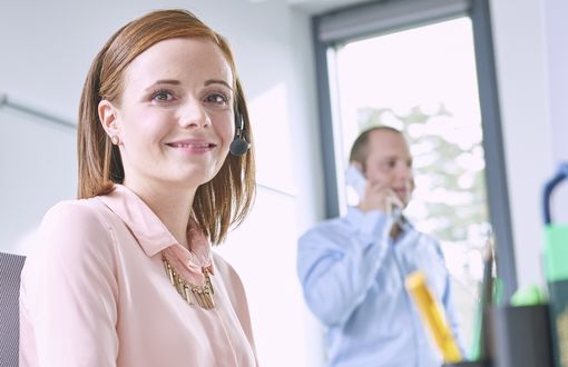 Eine Sachbearbeiterin des Personalservice führt am Headset ein Kundengespräch und lächelt freundlich in die Kamera.