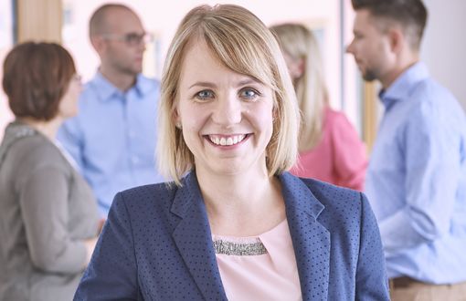 Eine Bewerberin steht nach einem erfolgreichen Bewerbungsgespräch beim KVS am Tisch und lächelt in die Kamera.